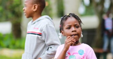 selective focus photography of girl biting her pendant beside a boy in gray pullover hoodie
